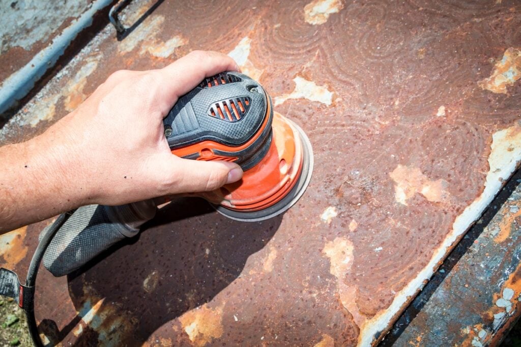 how to get rid of rust on metal Man's hand operates a disc/orbital sander, to remove paint and rust from metal doors