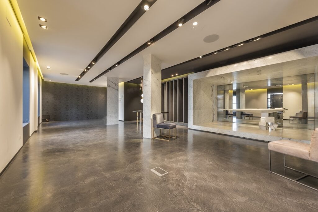 how to polish concrete floors An empty retail space with polished concrete floors and ceiling lighting fixtures, some loose furniture and little else