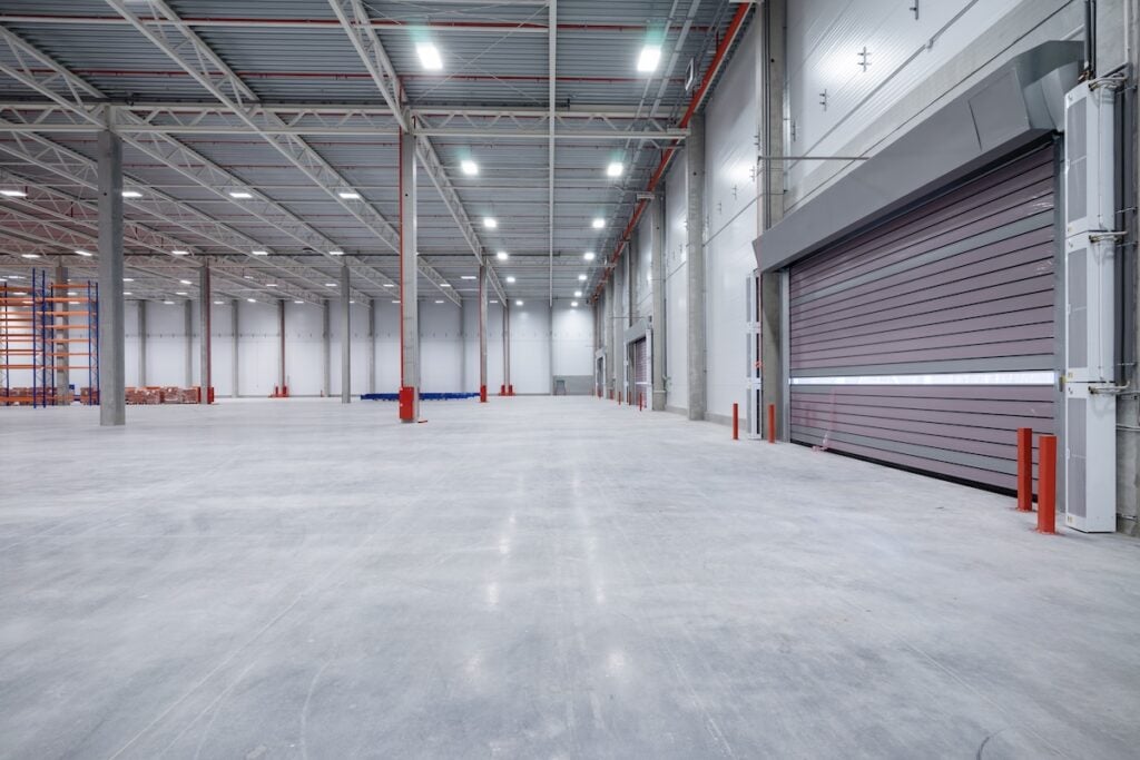large-scale epoxy flooring installation warehouse or hangar. Industrial building interior consist of polished concrete floor and closed door for product display or industry background.