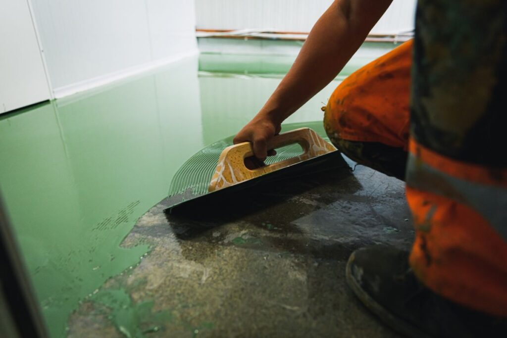 heat resistant paint for metal worker spreading green epoxy paint on floor