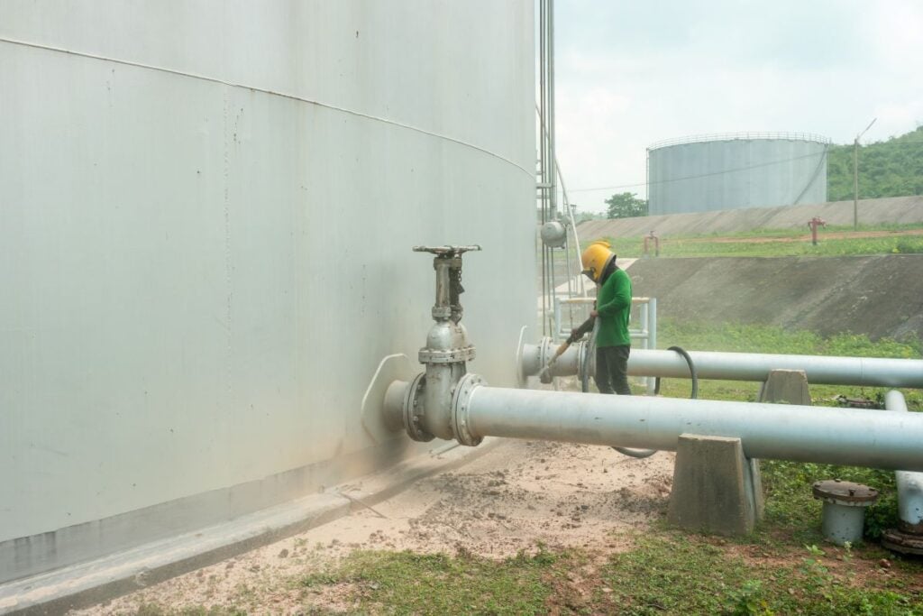 sandblasting worker preparing huge industrial tank for painting