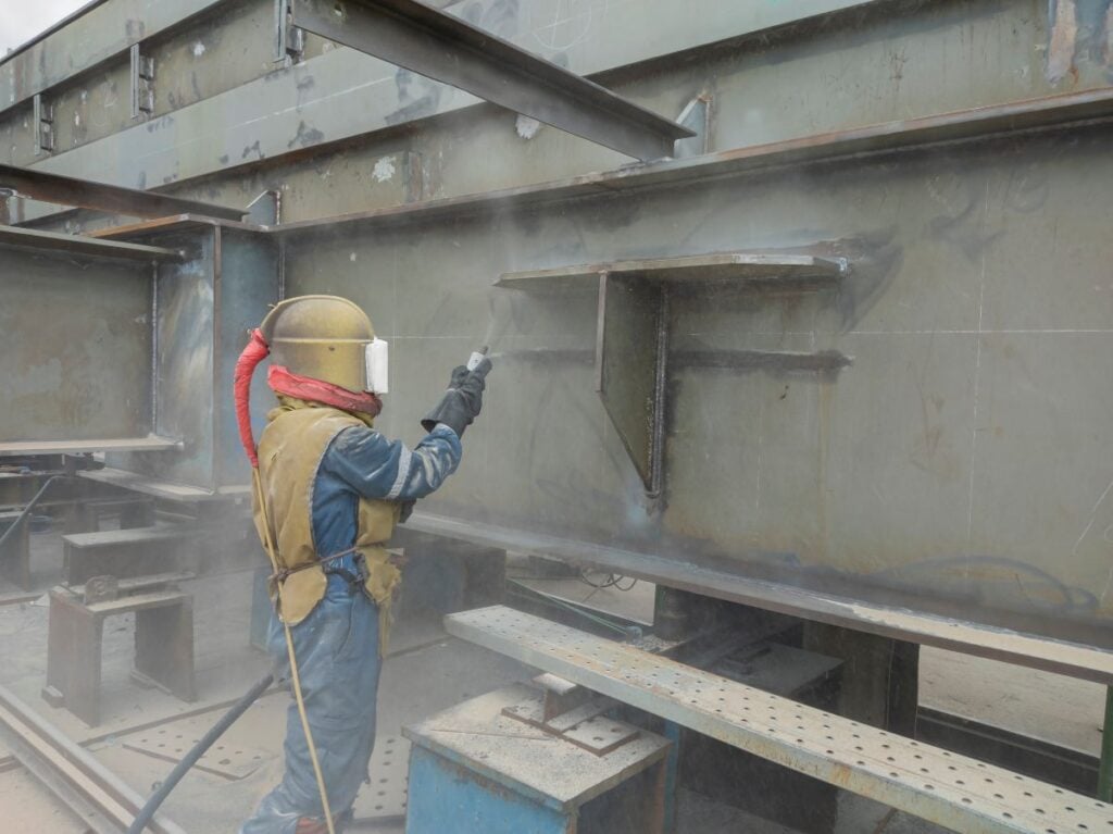 sandblasting worker using hose to clean green surface