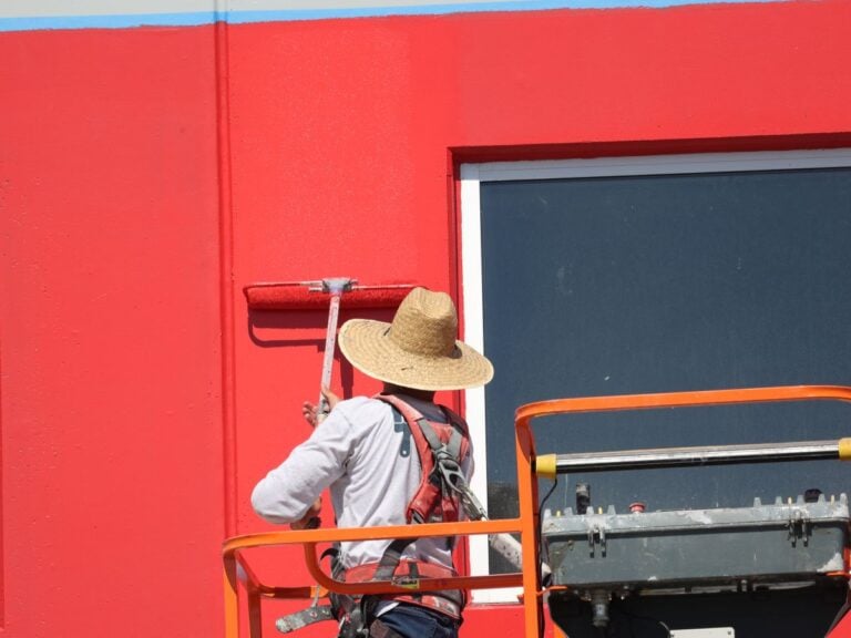 surface preparation for painting McLean worker paiting red building standing on platform