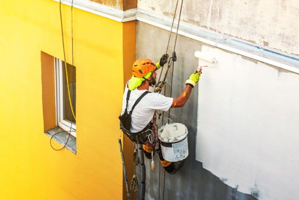 surface preparation for painting worker hanging on security cables painting white wall building