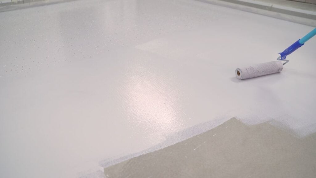 A worker paints the concrete floor with a roller white