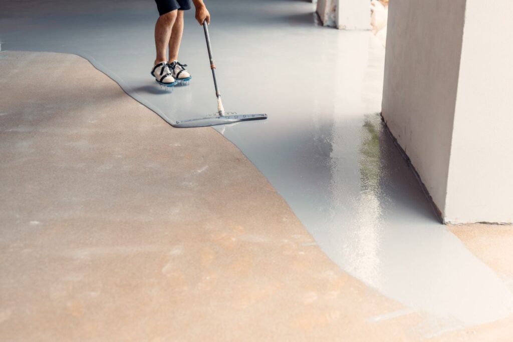 Construction worker applying epoxy resin flooring in industrial building