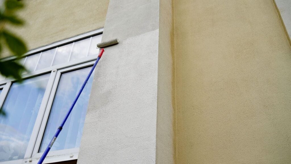 Construction worker is painting a building using a paint roller on a telescopic handle