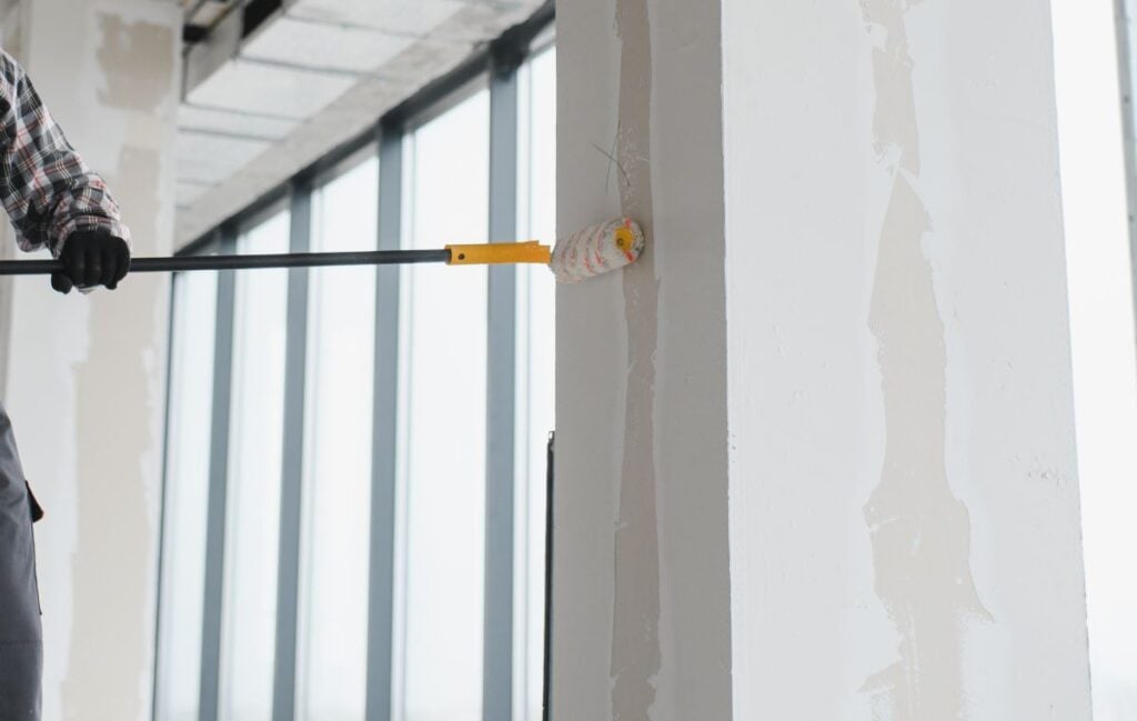 Construction worker painting wall with roller in building under construction