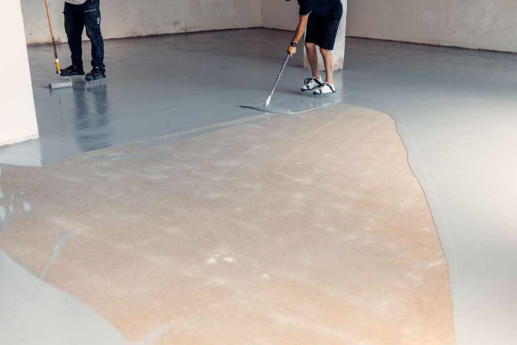 Construction workers applying grey epoxy resin in an industrial hall