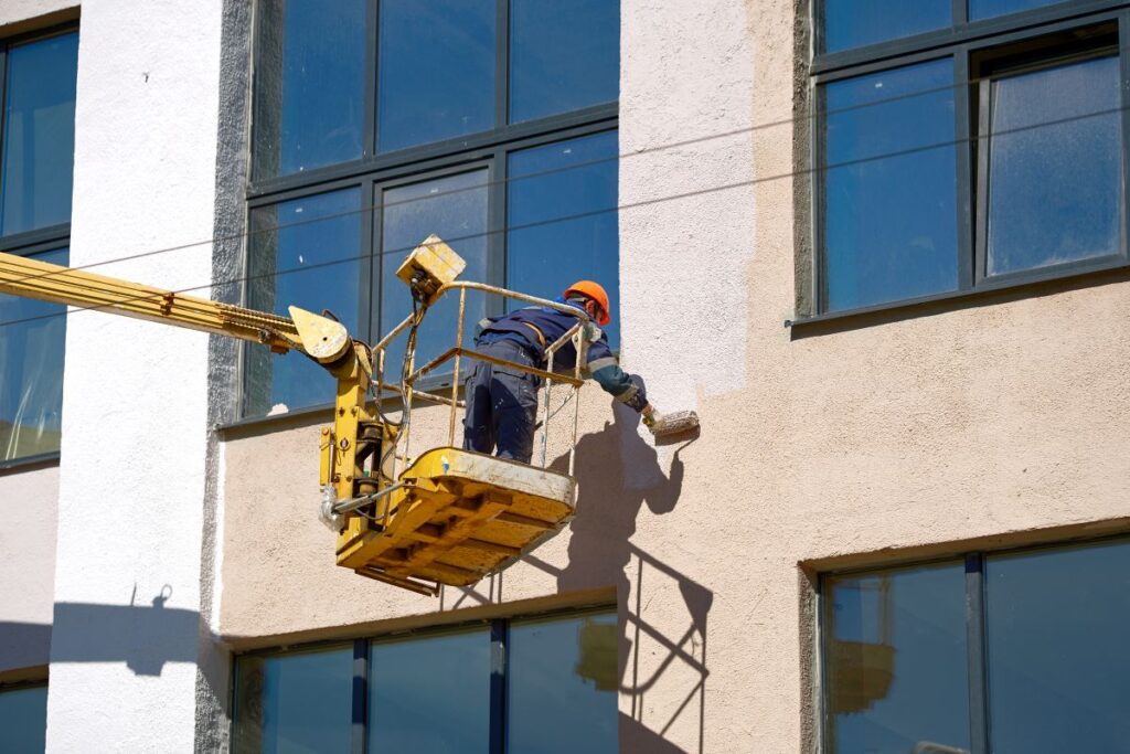 Man paint wall with brush roller in lifting bucket