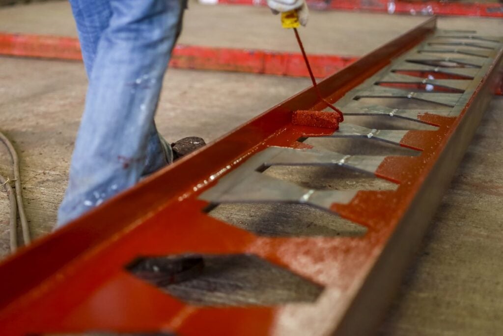 Person is painting metal structure with red paint using roller