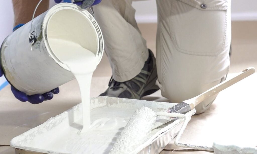 Professional interior construction worker pouring white color paint to tray