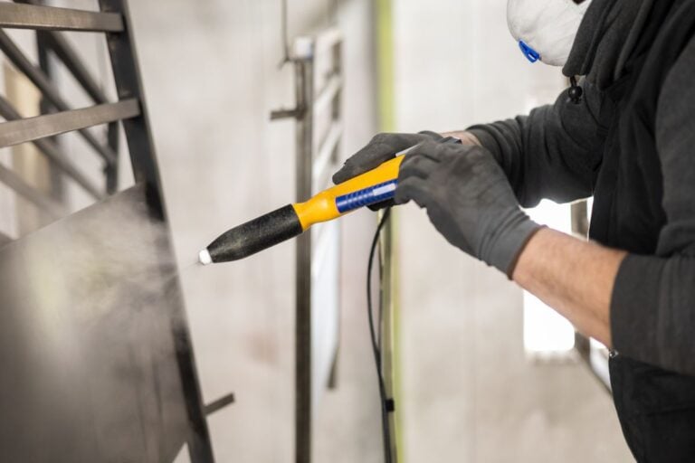 The detail of a man working in a factory finishes a job using the technique of electrostatic powder coating with a spray gun