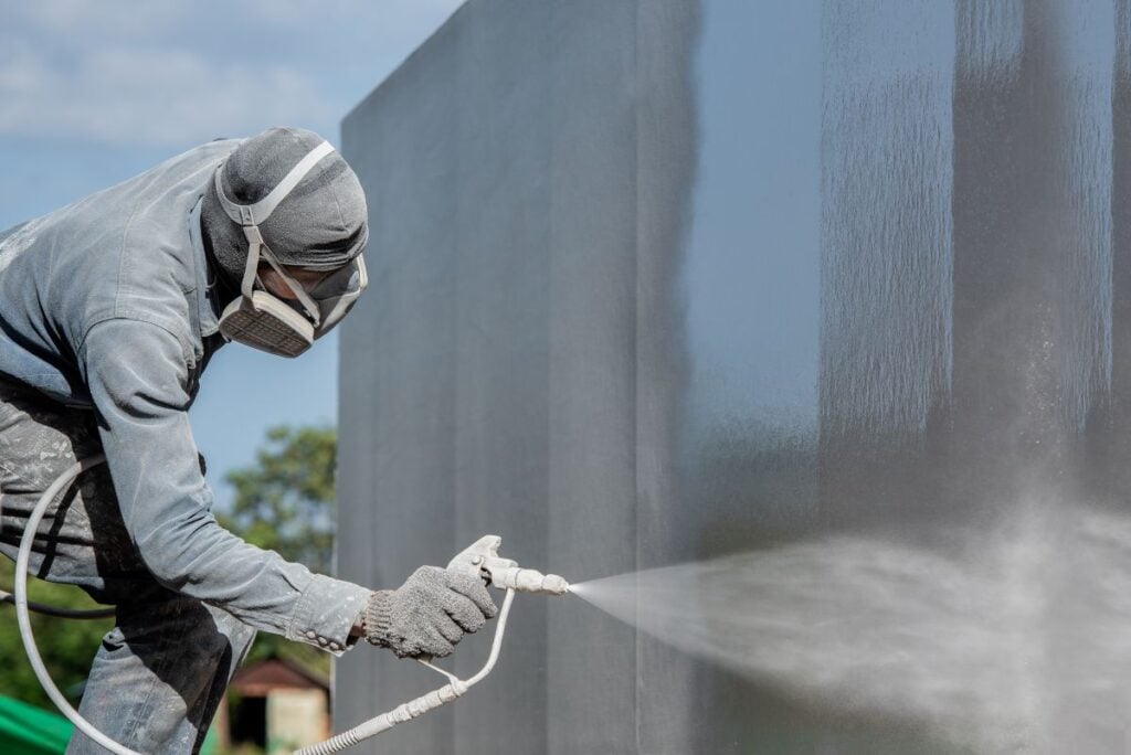 Worker painting on steel wall surface by airless spray gun