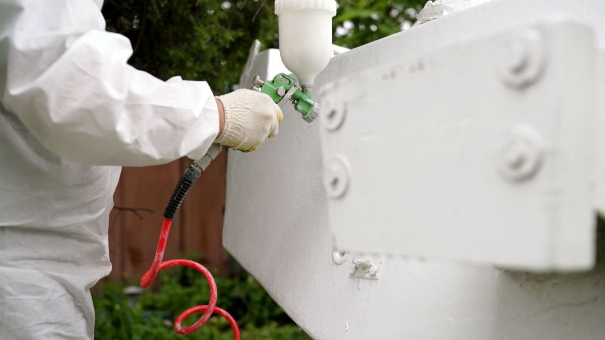 Worker spray painting metal surface with white paint
