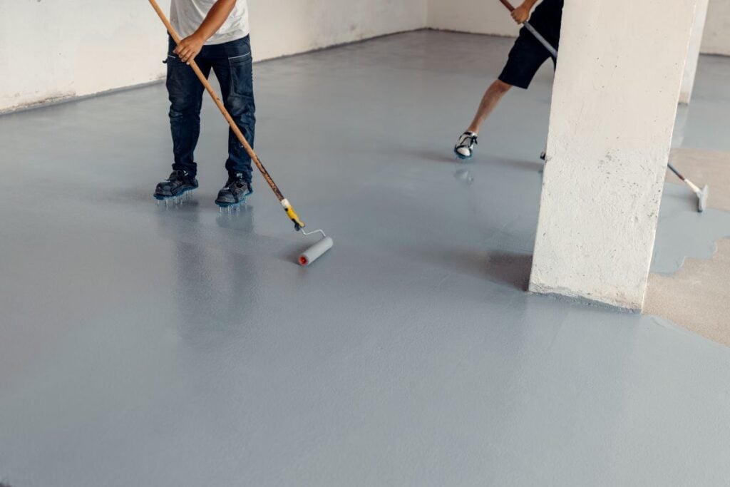 Workers applying epoxy flooring using rollers in a new industrial hall