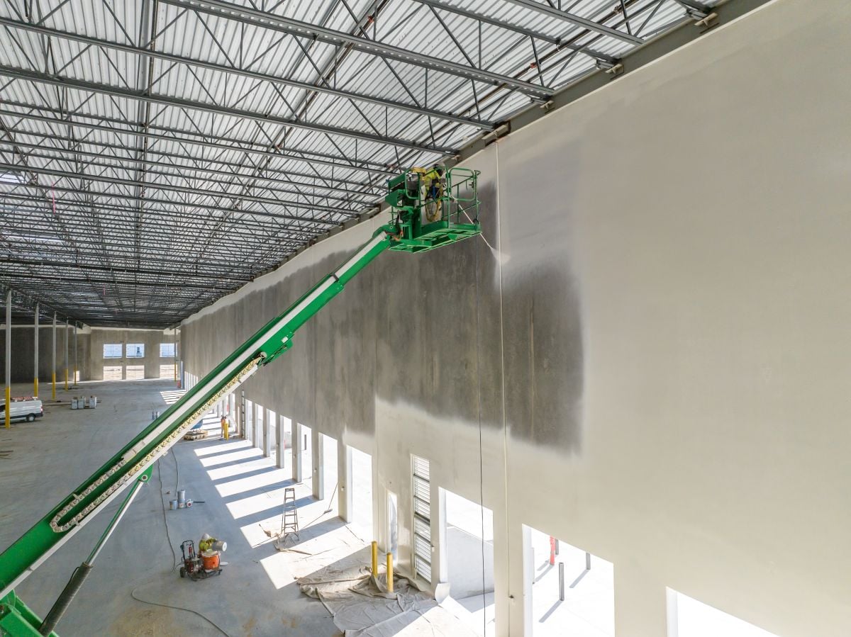 worker painting the interior of the warehouse with a paint sprayer on a forklift