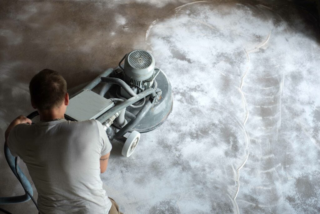 how to clean concrete floors Construction worker in a family home living room that grind the concrete surface before applying epoxy flooring.Polyurethane and epoxy flooring.Concrete grinding.