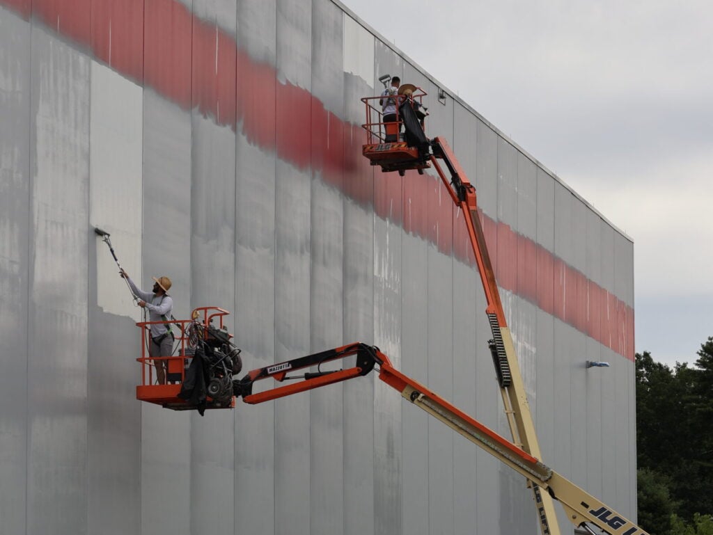 how much do painters charge per square foot two workers standing on elevated platform using red paint