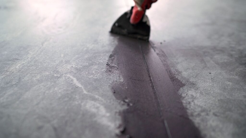 Construction professional carefully spreading dark sealant along concrete expansion joint using specialized trowel during detailed repair and maintenance process