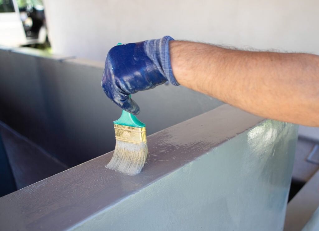 Worker Applying Waterproof Coating to Concrete Parapet With Brush