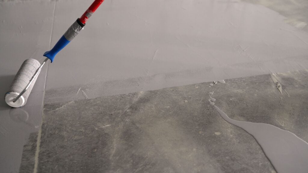 parking garage floor coating Painting the floor with a roller. Worker and repair work. Applying an anti-slip layer to the floor of an underground parking lot. A construction worker applies gray epoxy resin in an industrial hall.