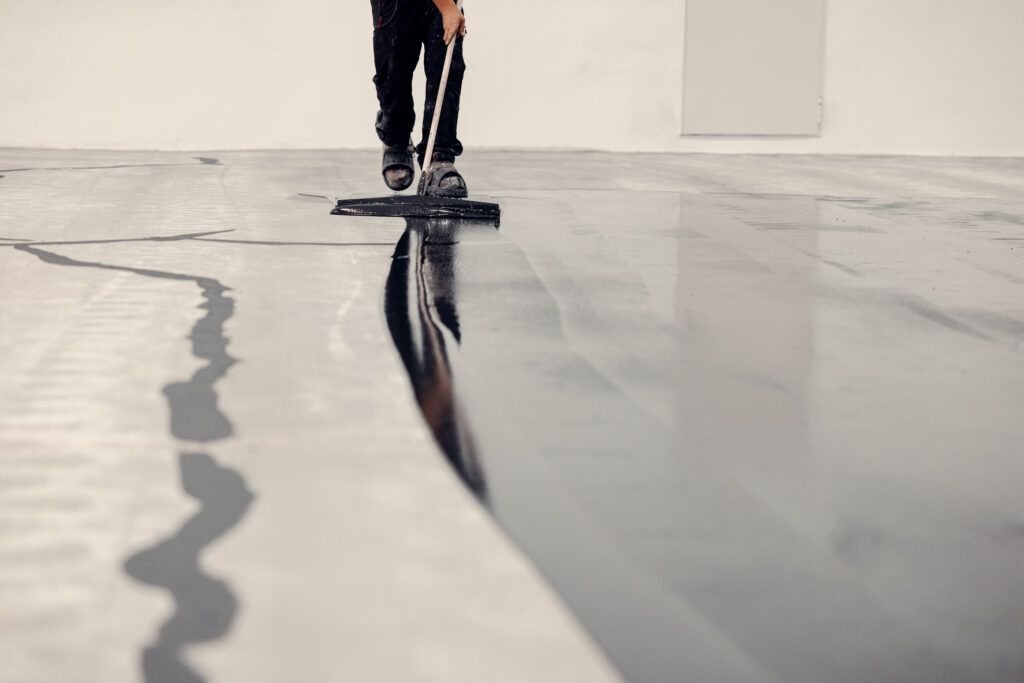Worker applies grey epoxy resin to a new floor