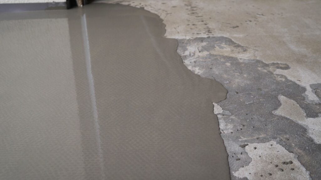 Filling floor with self-leveling concrete mix, covering damaged surface, creating smooth and even base
