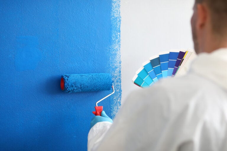 painting occupied office building Craftsman holds roller and a color palette and paints white wall blue. Wall painting services and painting concept