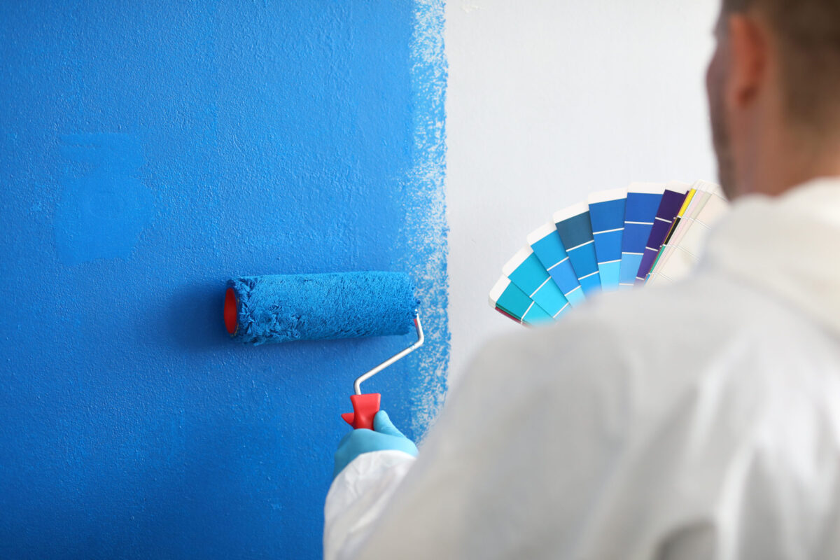 painting occupied office building Craftsman holds roller and a color palette and paints white wall blue. Wall painting services and painting concept
