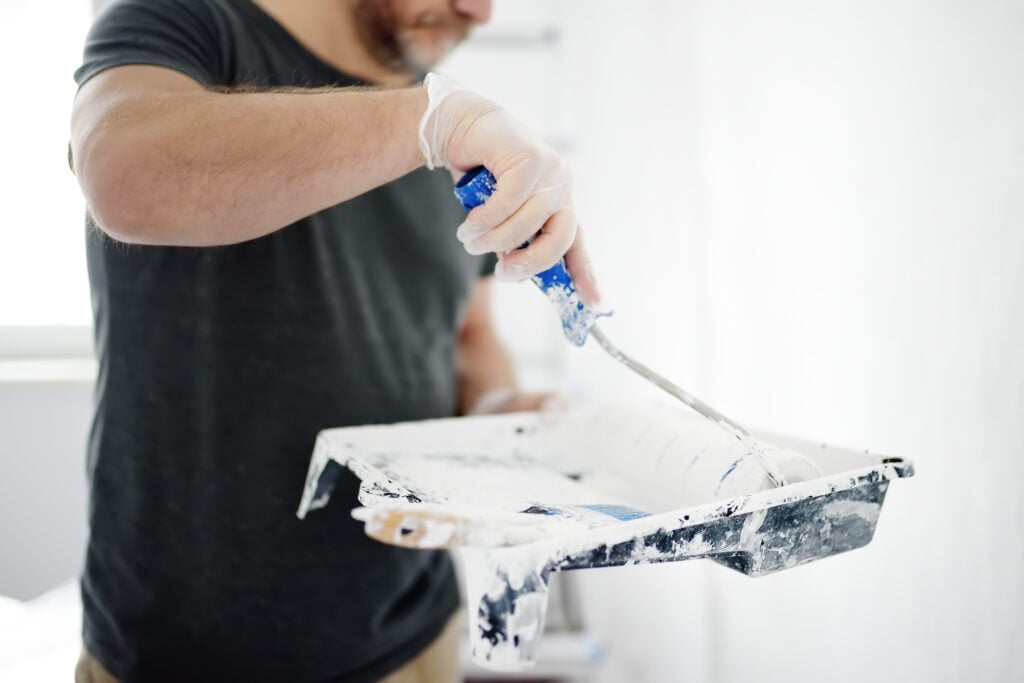 Mature man making repairs in the apartment. The person paints the wall white with roller. Do it yourself. DIY. Repair with their hands.